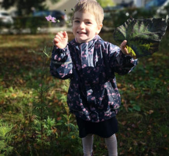 Kind im Herbst auf einer Wiese, hält Blätter in den Händen