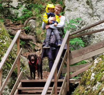 Erwachsene Person trägt ein Kind eine Holztreppe hinunter, daneben ein Hund
